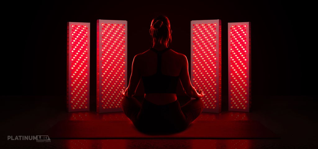 Woman in the dark in a meditative pose in front of panels of red lights